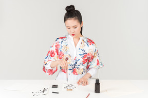 Young woman in a colourful japanese kimono learns calligraphy by drawing a hieroglyph