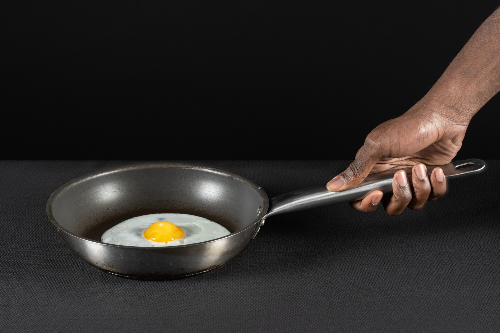 Human arm holding a fried egg on pan