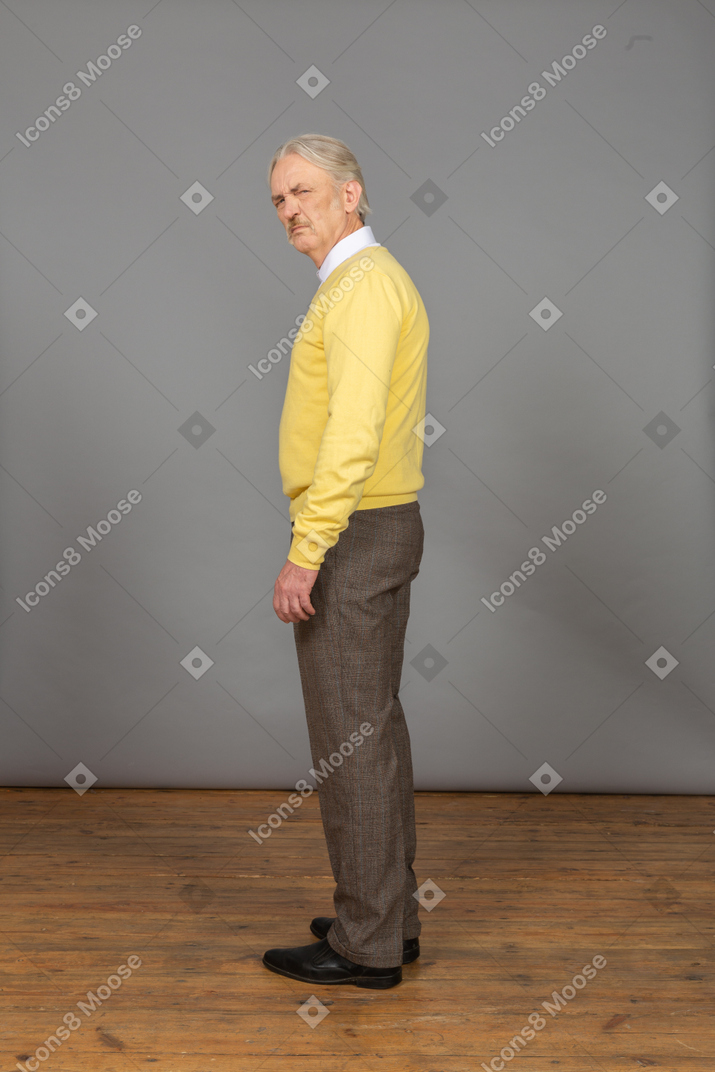 Вид сбоку на недовольного старика в желтом пуловере, смотрящего в камеру