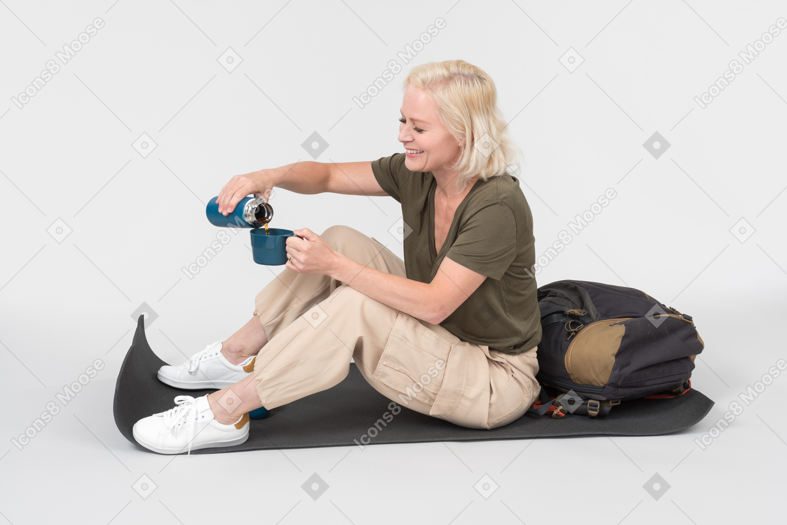 Mature female tourist sitting on tourist mat and passing on cup