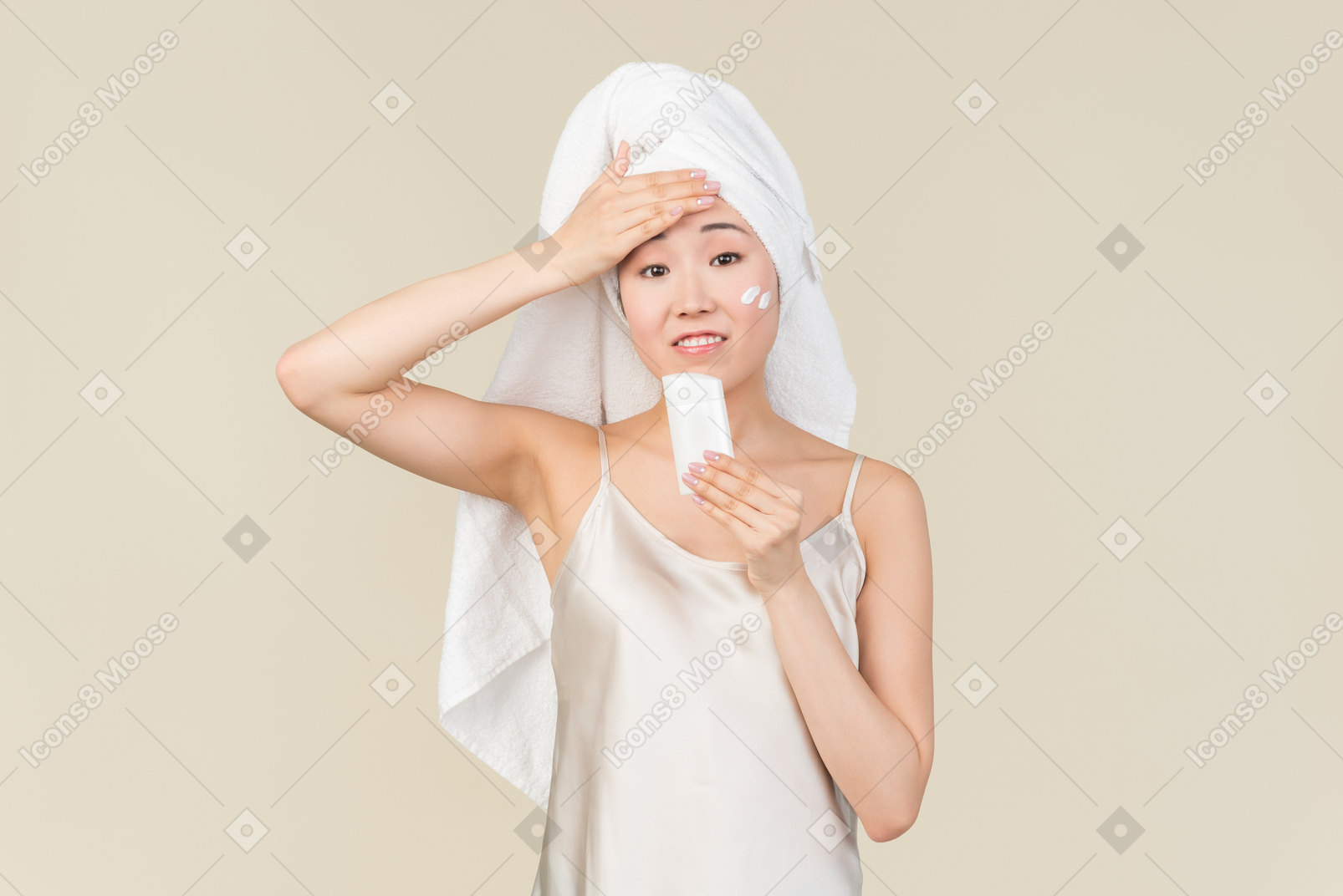 Asian woman with hair wrapped in towel holding cream and touching head