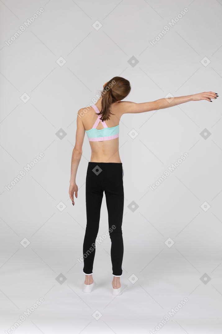 Vista posterior de una jovencita en ropa deportiva extendiendo su mano e inclinando la cabeza