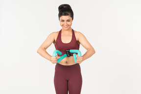 Young indian woman in sportswear holding hand expander