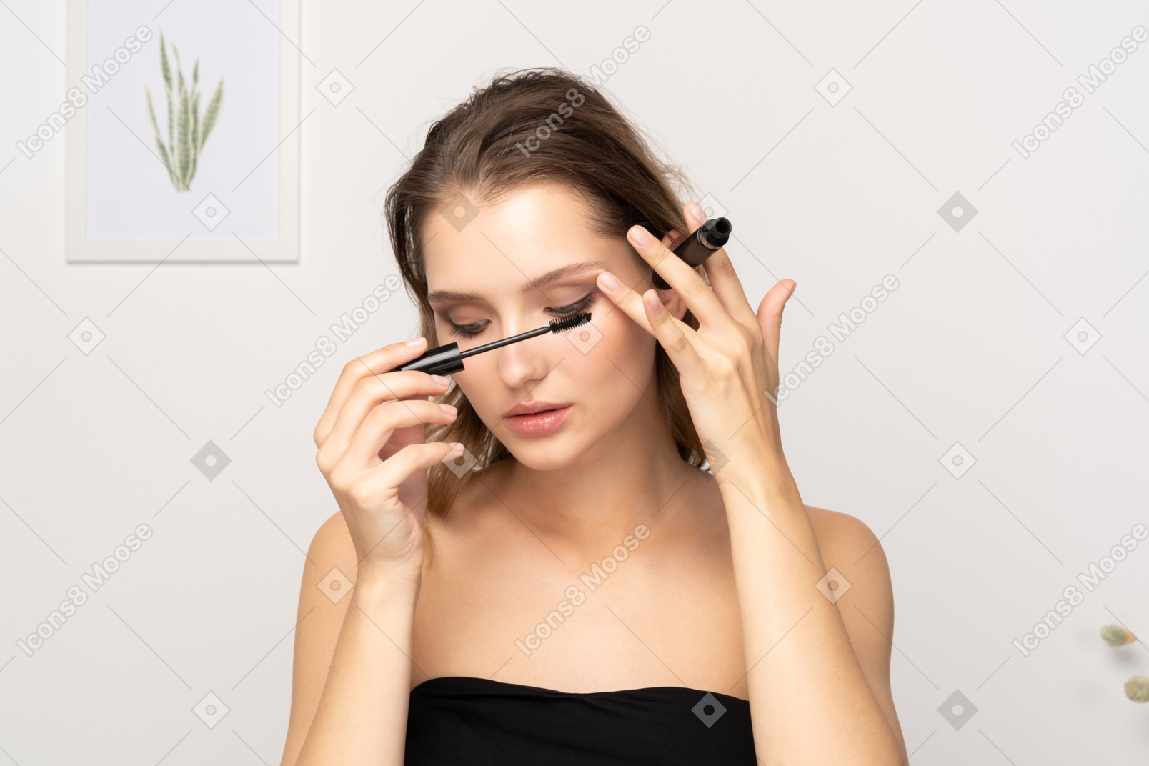Vista frontale di una giovane donna che indossa un top nero che applica il mascara