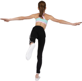 Vista posteriore di una ragazza adolescente in abiti sportivi in equilibrio sulla gamba