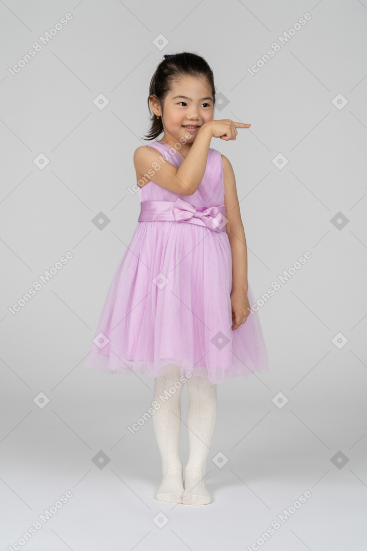 Front view of a little girl in a tutu dress smiling while pointing left