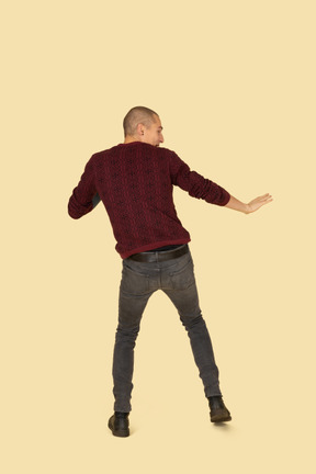 Back view of a scared unwilling young man dressed in red pullover outstretching his hands