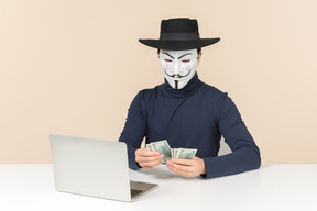 Pirate informatique portant masque de vendetta comptant l'argent