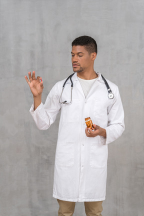 Young doctor with stethoscope looking at pill