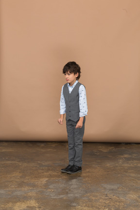 Вид спереди мальчика в костюме, стоящего со сжатыми кулаками