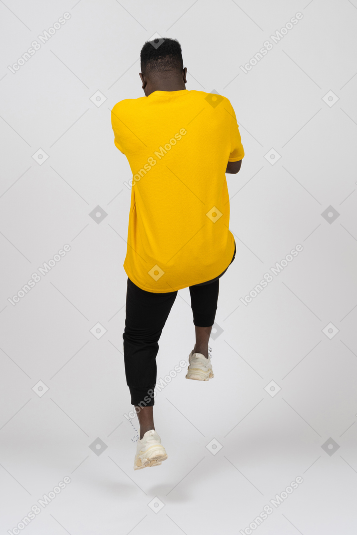 戻ってジャンプする黄色のtシャツを着た若い浅黒い肌の男の背面図