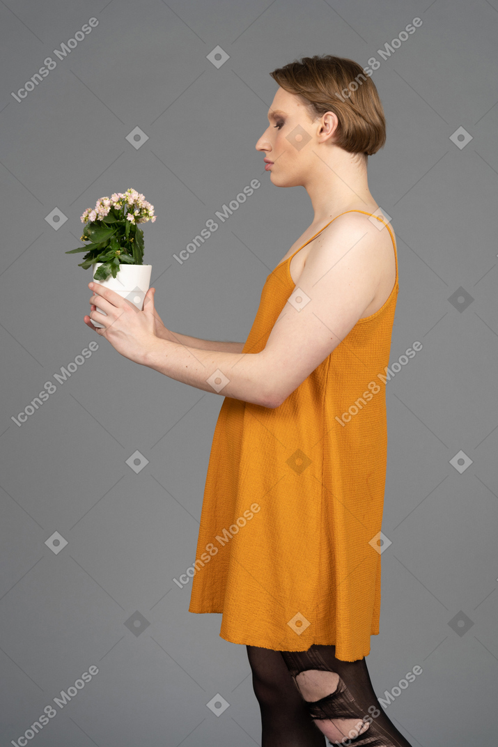 Junge queere person in orangefarbenem kleid mit blumentopf