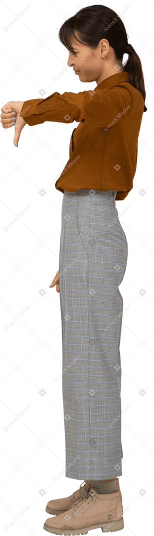 Vista lateral de uma jovem mulher asiática de calça e blusa mostrando o polegar para baixo