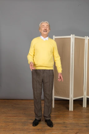 Front view of an old smiling man gesticulating with his eyes closed