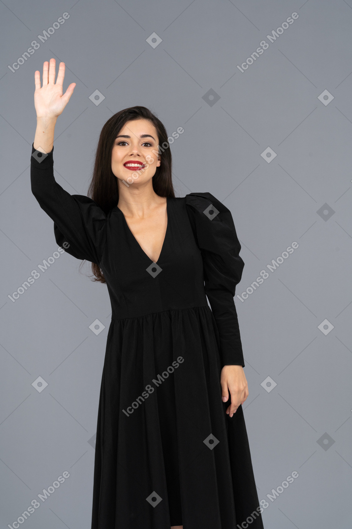 Vista frontal de un saludo sonriente señorita en un vestido negro