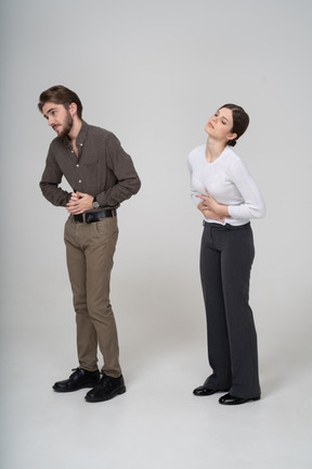 Three-quarter view of a young couple in office clothing touching stomach