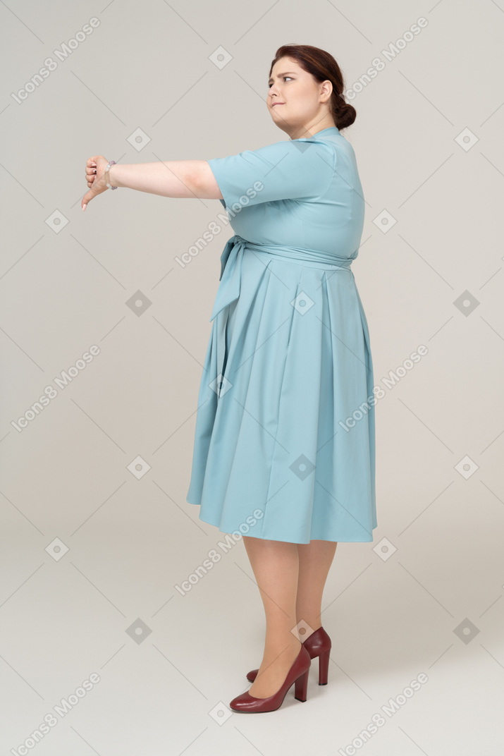 Vue latérale d'une femme en robe bleue montrant le pouce vers le bas
