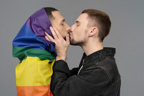 Gros plan d'un jeune homme embrassant un autre homme enveloppé dans un drapeau lgbt