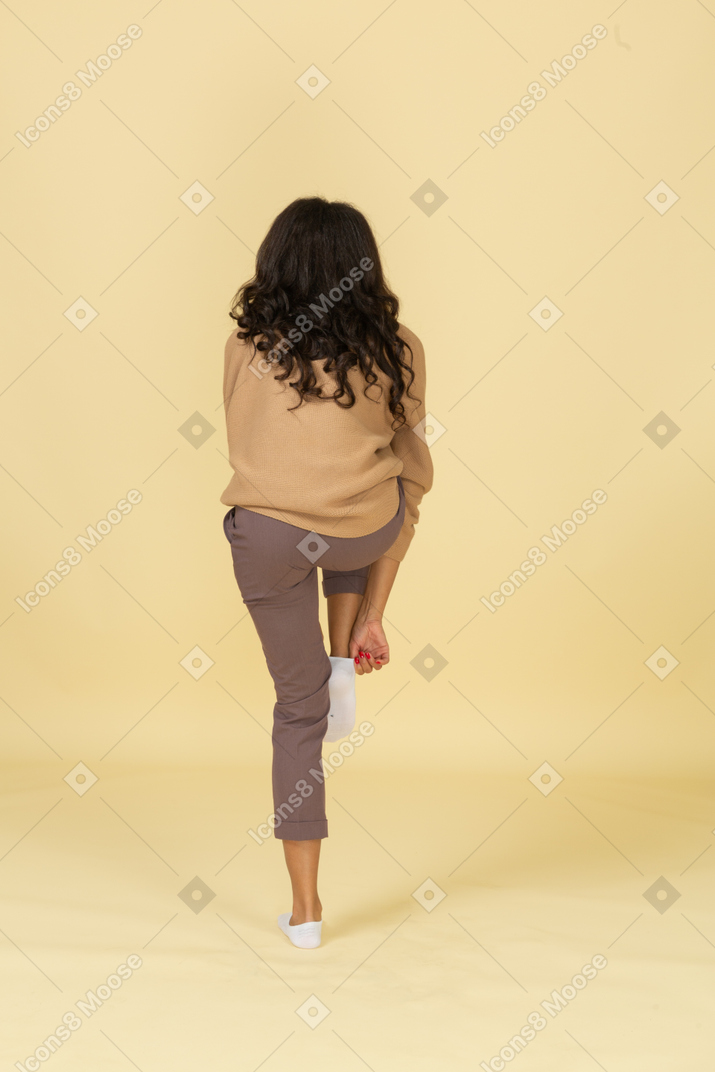 Back view of a tired dark-skinned young female putting on a sock