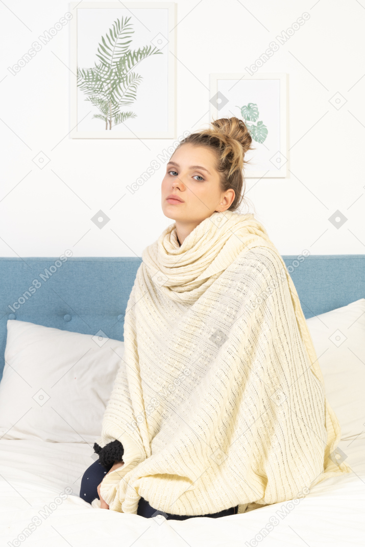 Three-quarter view of a young lady wrapped in white blanket sitting in bed