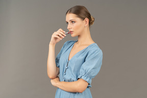 Vista di tre quarti di una giovane donna in abito blu che applica un rossetto