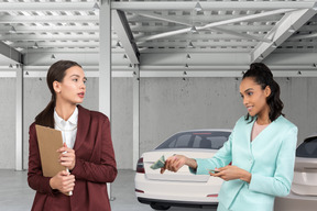 Woman giving dollar bills to another woman in parking garage