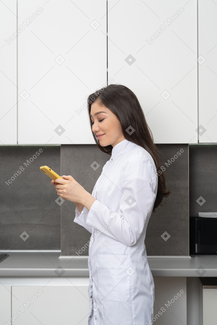 Vista laterale di una dottoressa felice guardando il suo telefono