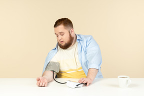 テーブルと血圧チェックに座っている若い太りすぎの人を心配しています。
