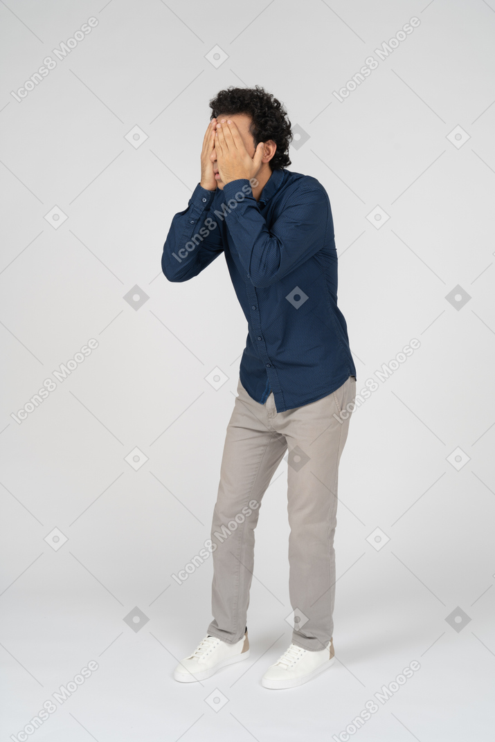 Vista frontal de um homem com roupas casuais cobrindo o rosto com as mãos