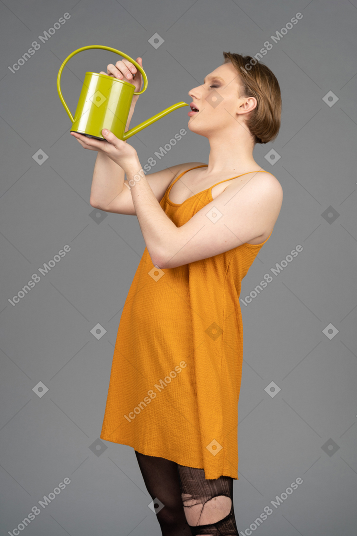 Side view of a young genderqueer person drinking from watering can