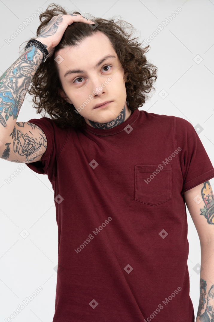 Adolescente tatuato che tiene i suoi capelli castani ricci con una mano