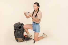 Empörte junge asiatische frau, die nahen rucksack steht und foto mit smartphone macht