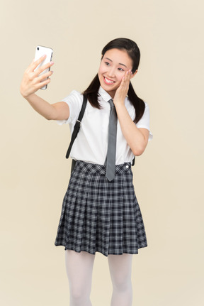 Menina da escola asiática tocando o rosto e fazendo um selfie