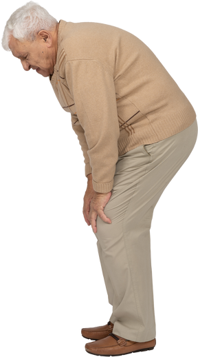 一位身穿休闲服的老人弯下腰，抚摸受伤的膝盖的侧视图