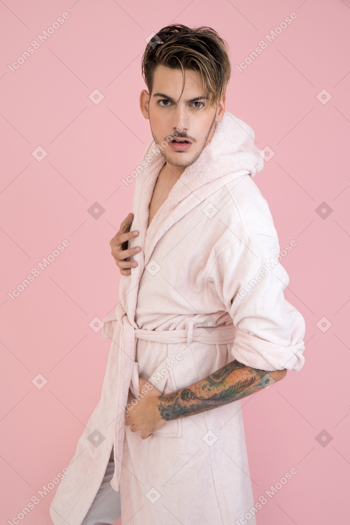 Handsome young guy standing in pink robe and watching to the camera closely