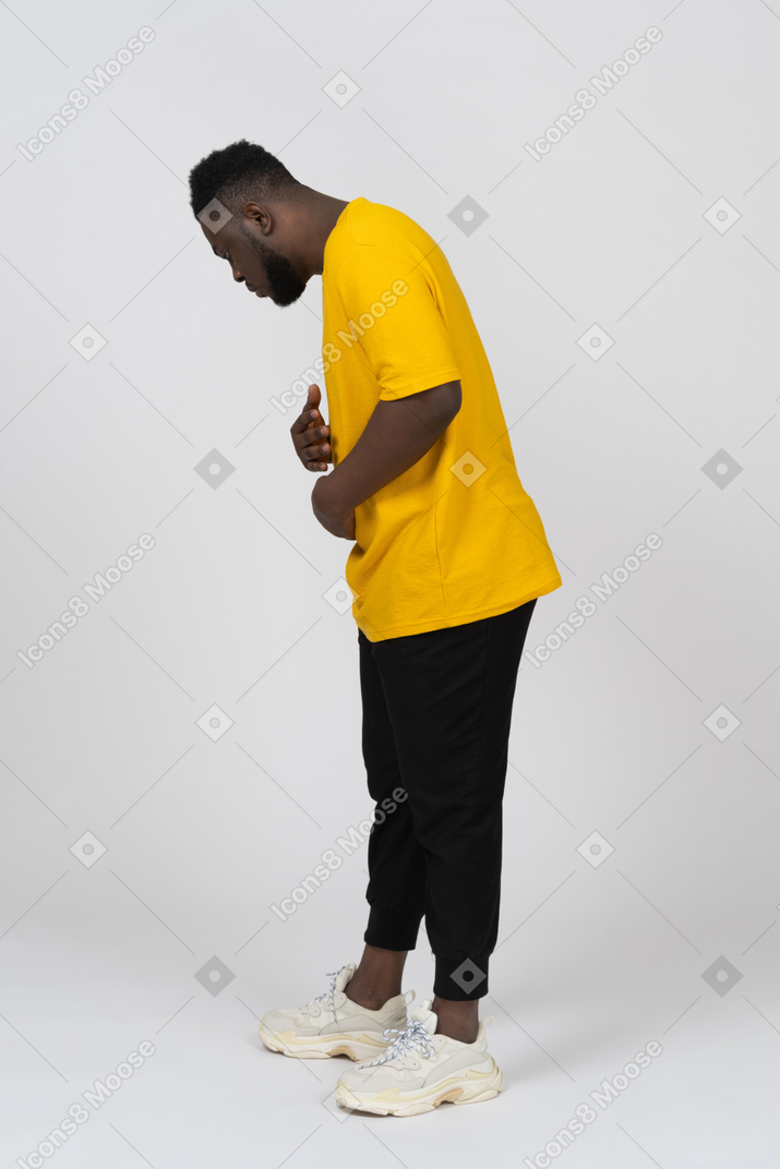 Vue latérale d'un jeune homme à la peau foncée en t-shirt jaune touchant l'estomac et regardant vers le bas