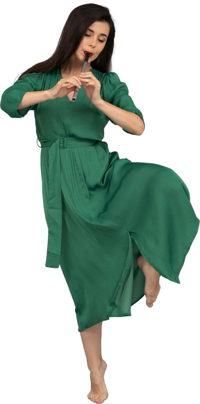 Vue de face d'une jeune femme dansante en robe verte jouant de la flûte