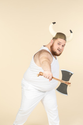 Un hombre de talla grande de color blanco con un casco con cuernos en la cabeza, sosteniendo un hacha de doble hoja