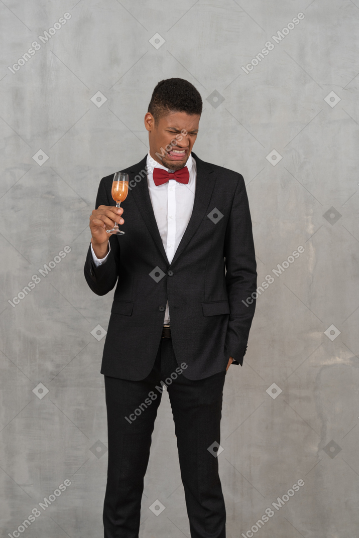 Молодой человек с сморщенным лицом держит бокал шампанского