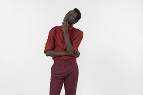 Un joven negro con una camisa roja con mangas enrolladas y pantalones rojo oscuro de pie solo sobre el fondo blanco.