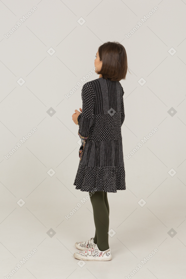 Three-quarter back view of a confused little girl in dress holding hands together