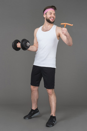 Cheerful man with a dumbbell looking with love at a sausage in his hand