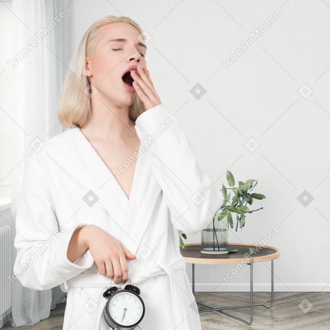 A woman in a white bathrobe is waking up with an alarm clock