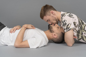 Deux jeunes hommes de race blanche allongés sur le sol l'un surplombant l'autre et s'embrassant doucement