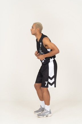 Vista lateral de um jovem jogador de basquete masculino surpreso tocando o estômago