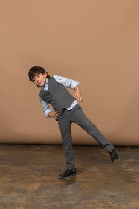 Front view of a boy in suit balancing on one leg with hands on hips