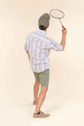 Young caucasian man holding tennis racket and standing back to camera