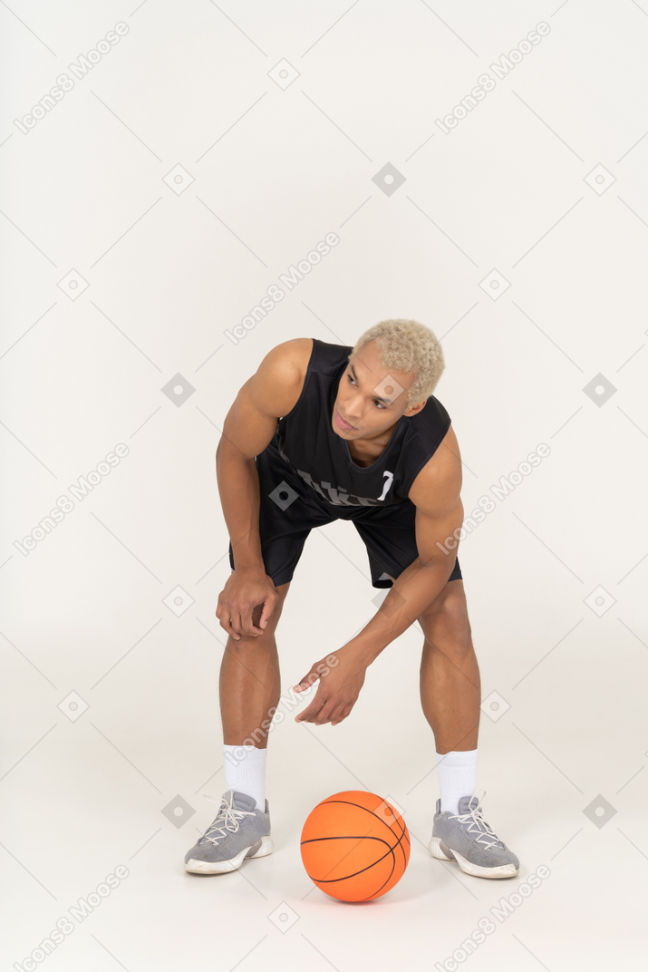 Vista frontal de un joven jugador de baloncesto masculino de pie junto a la pelota