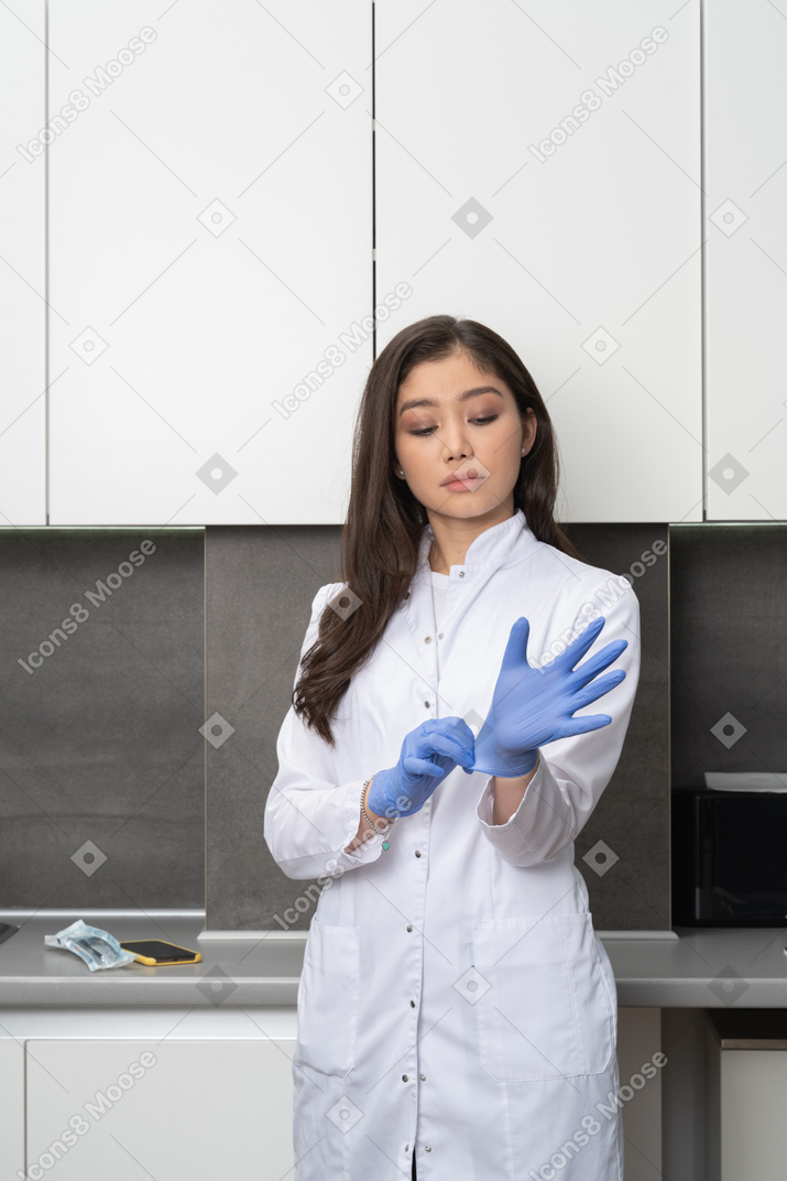 Front view of a young female putting on protective gloves and looking down
