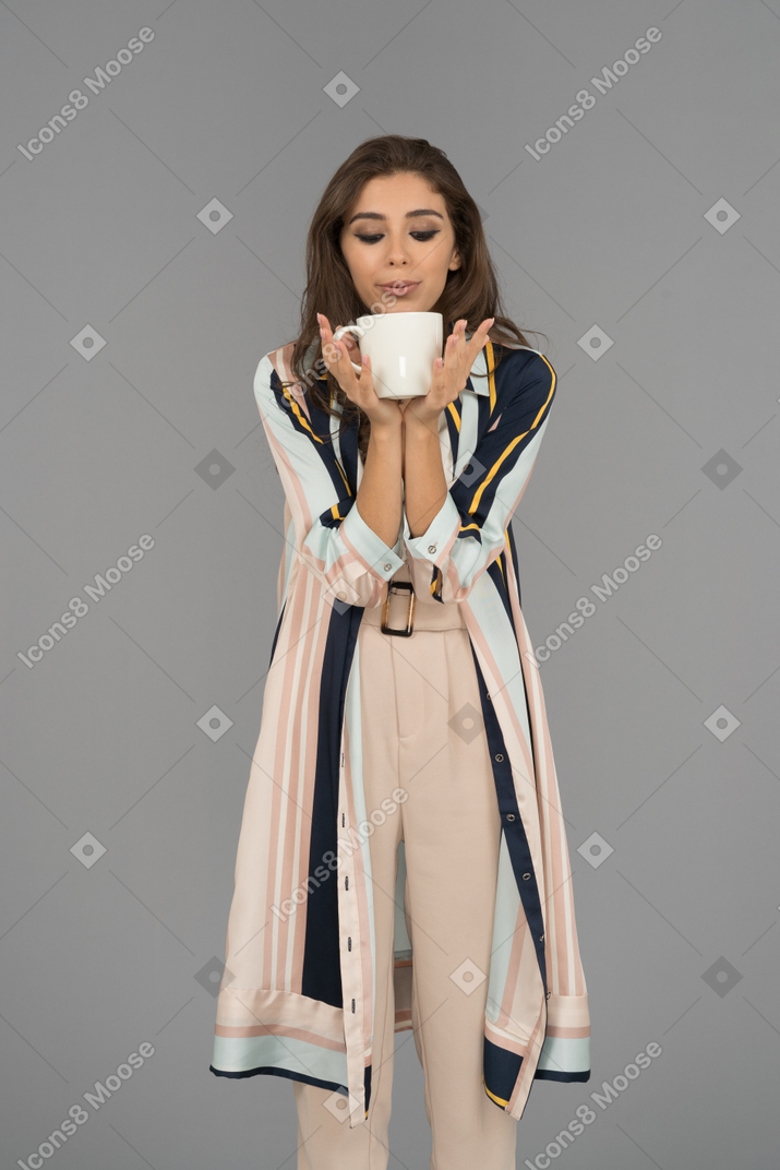 迷人的年轻女子，拿着一杯热茶，吹在它上面
